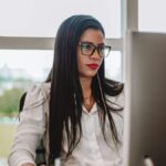 Focused woman with glasses working at a desk in an office environment.